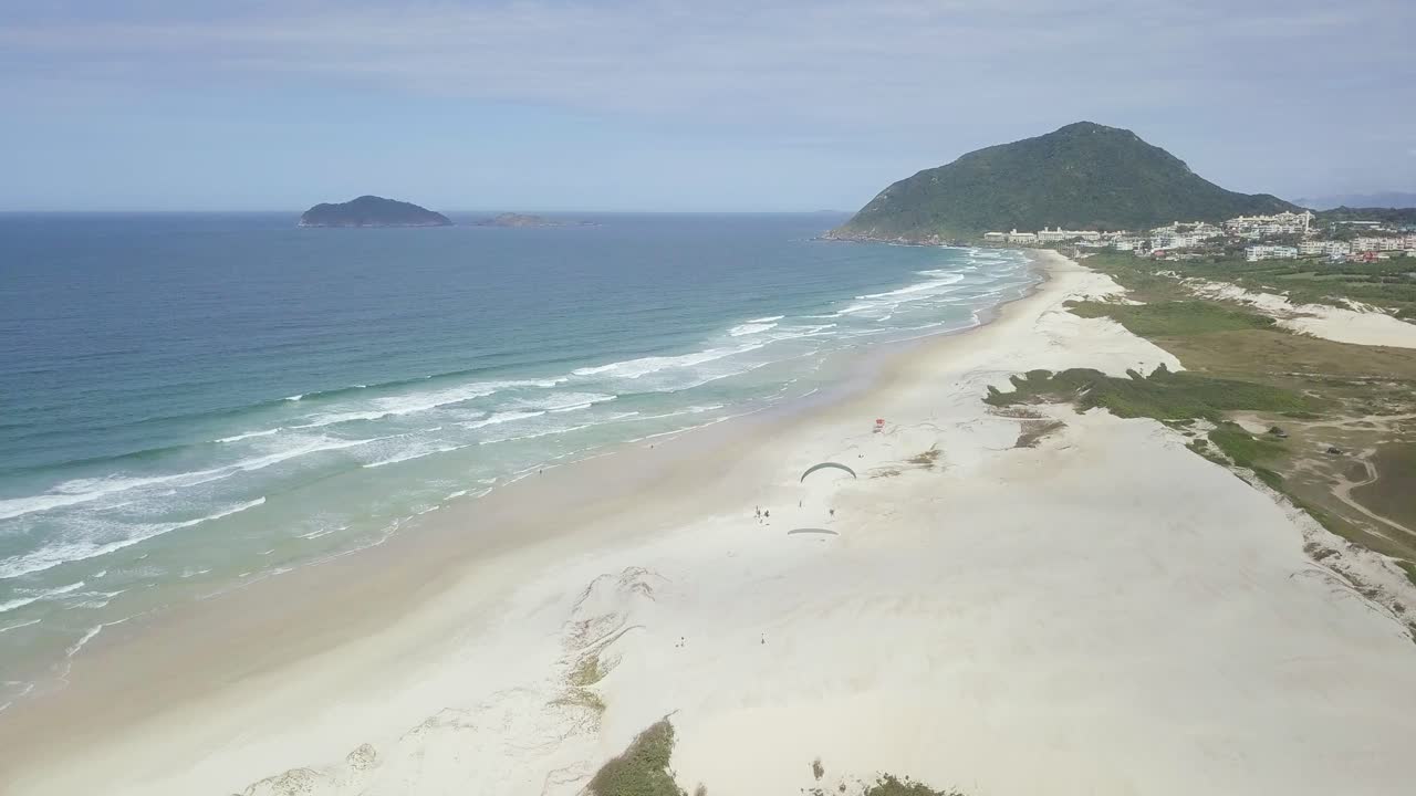 파란 하늘을 배경으로 해변에 상륙하는 파라모터 조종사의 4k 공중 추적 샷