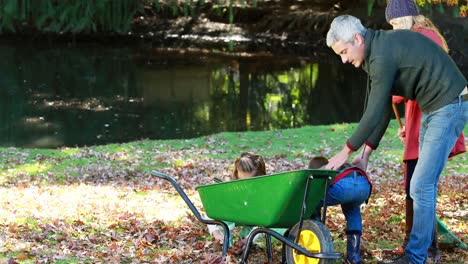 family picking up autumn leaves and putting in a wheelbarrow