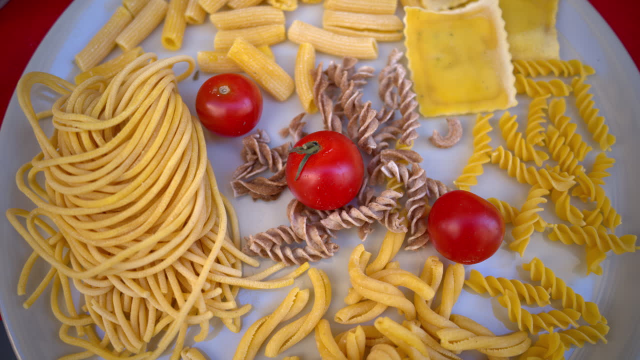 White plate with a variety of uncooked pasta, noodles and cherry tomatoes on it