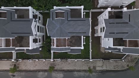 a newly constructed row of identical large white multi story villa styled houses along a suburban road