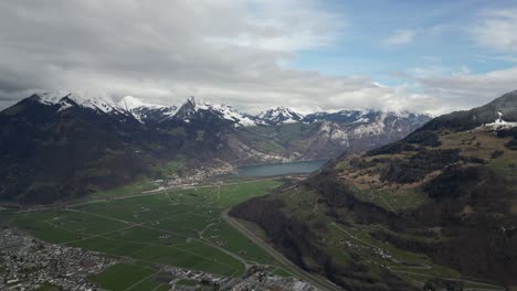 una foto aérea de gran altitud de glarus, suiza, revela sus alrededores envueltos por picos de montañas cubiertos de nieve, con un lago sereno añadiendo al pintoresco telón de fondo