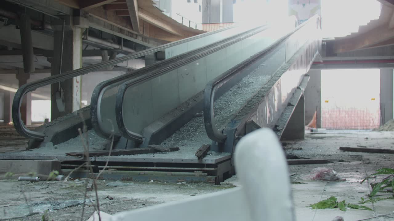 Destroyed escalator in abandoned shopping center mall with debris and exposed structure.