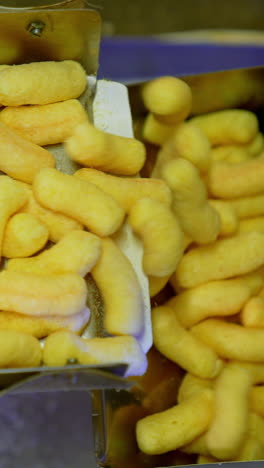metal boxes at conveyor belt being filled with sweet snacks. production on maize crispy sticks at modern food plant. close up. vertical video