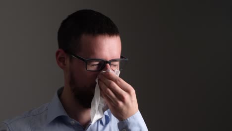 young sick man with glasses sneezes into a tissue paper - slow motion