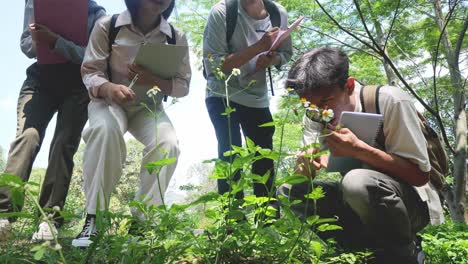 group of asian students learning and exploring nature together using magnifying glass