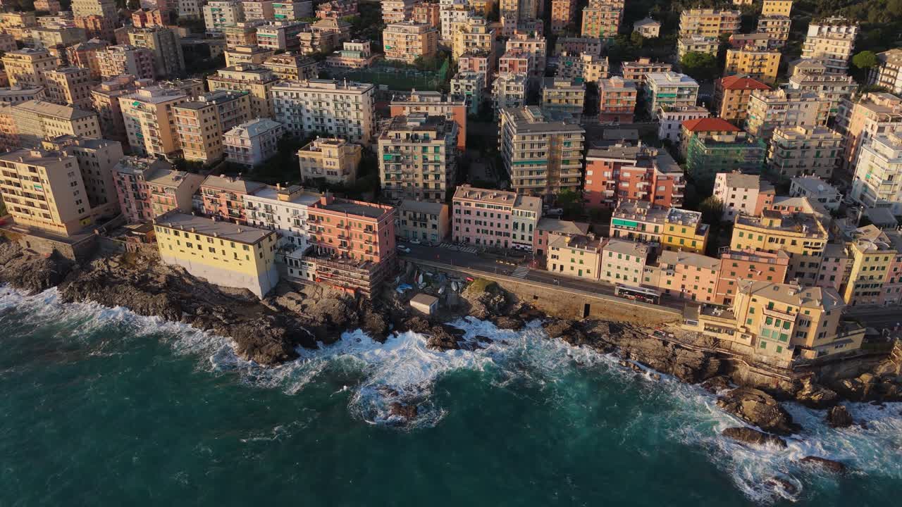 Genoa's colorful seaside houses and rugged coastline with crashing waves, aerial view
