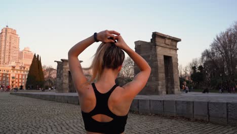 Mujer-En-Forma-Atándose-El-Pelo-Antes-Del-Entrenamiento-Físico-Al-Aire-Libre,-Desde-Atrás