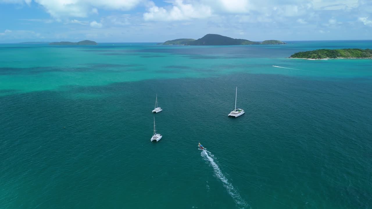 Drone orbits sailboats as a longtail speeds toward the Andaman off Rawai Beach, Phuket