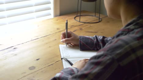 young puerto rican female writing feelings and memories in personal journal, over shoulder view