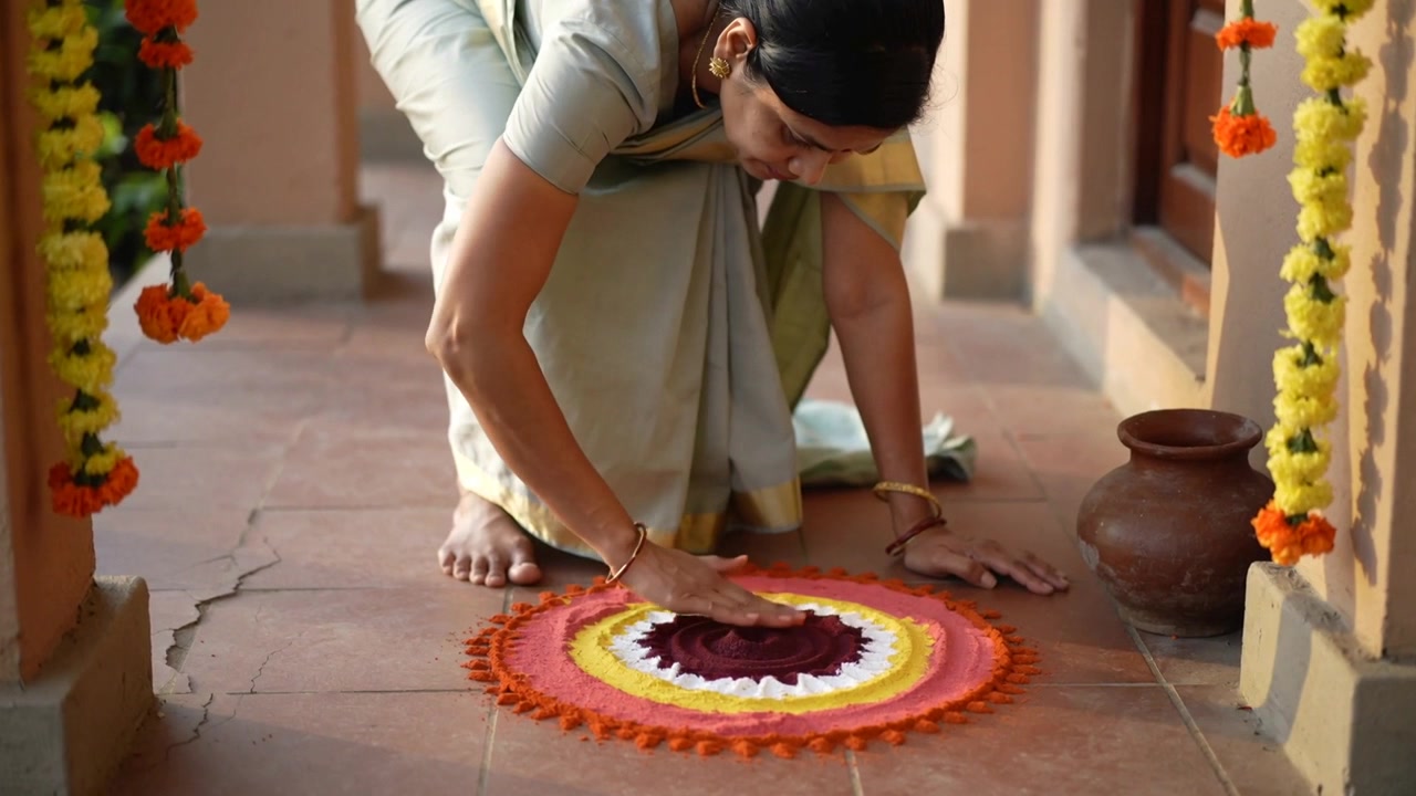 Donna indiana inginocchiata, in sari, che rifinisce un rangoli all'ingresso per la puja, posizionando la mano destra al centro.
