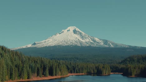 4k aerial snowy mountain with lake and evergreen hills in foreground drone dolly out