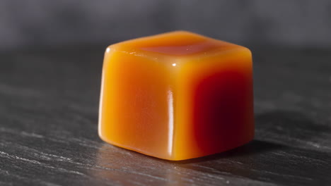 a single piece of glossy caramel candy on a dark surface