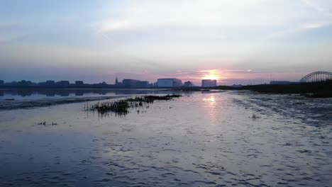 slow-drone-dolly-shot-of-a-reflection-of-the-sunrise-first-in-mud-later-in-the-water-in-the-netherlands-during-summertime