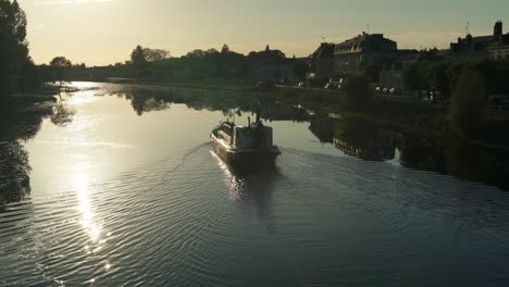 silhouette of small vessel sailing at night on a peaceful river next to a quaint village