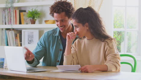 Pareja-Sonriente-En-Casa-Con-Una-Computadora-Portátil-Revisando-Las-Finanzas-Para-Iniciar-Juntos-Negocios-Independientes