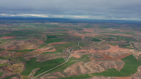 Vista-Aérea-Del-Paisaje-Desértico-Con-Una-Carretera-Y-Campos-Verdes-A-Gran-Altitud-En-España.