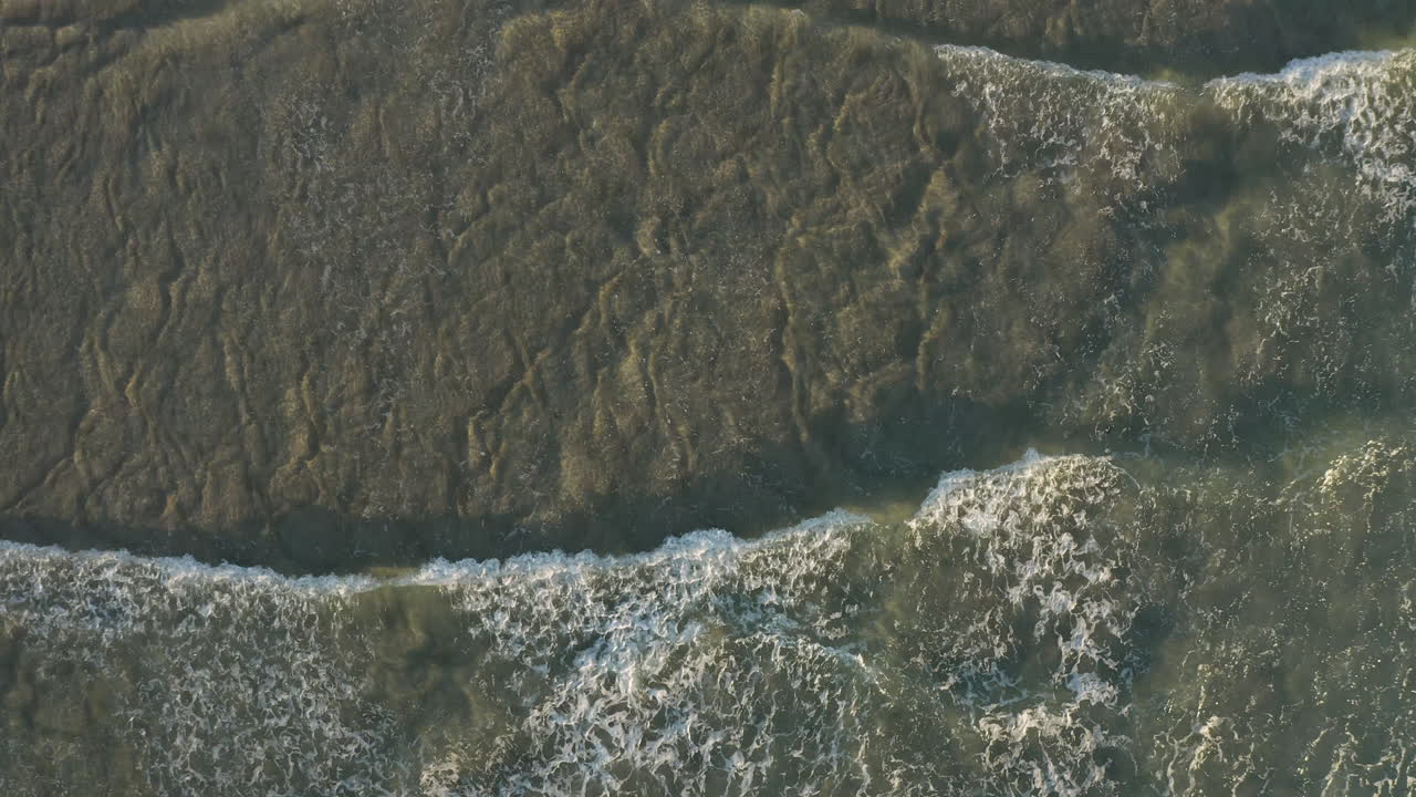 vista superior de 4k toma de drones de pequeñas olas, espuma y salpicaduras en el agua de mar del océano en un día soleado en byron bay, australia