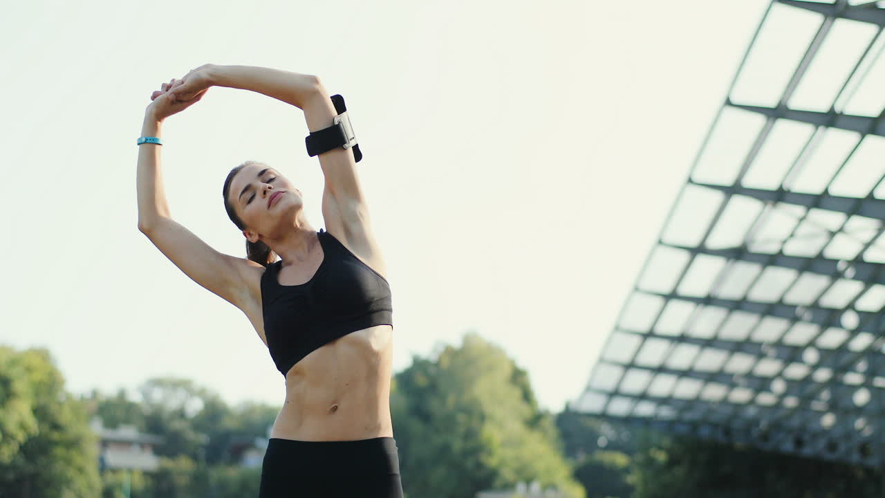 여름날 경기장에서 운동을 하고 손을 뻗는 젊은 조깅 여성