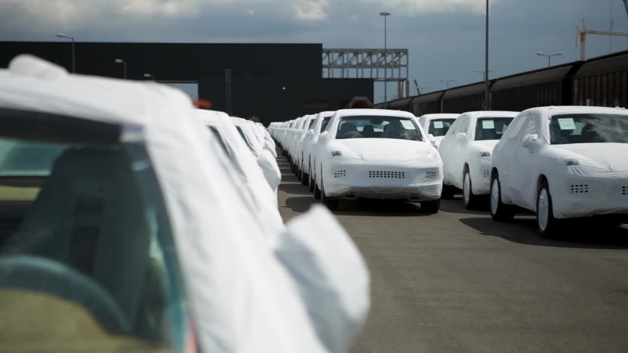 New cars wrapped in protective covers in a storage lot, ready for shipping