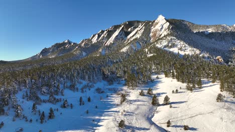 slow aerial drone rise with view of boulder flatirons at sunrise on a bright winter day with nature landscape and park in view