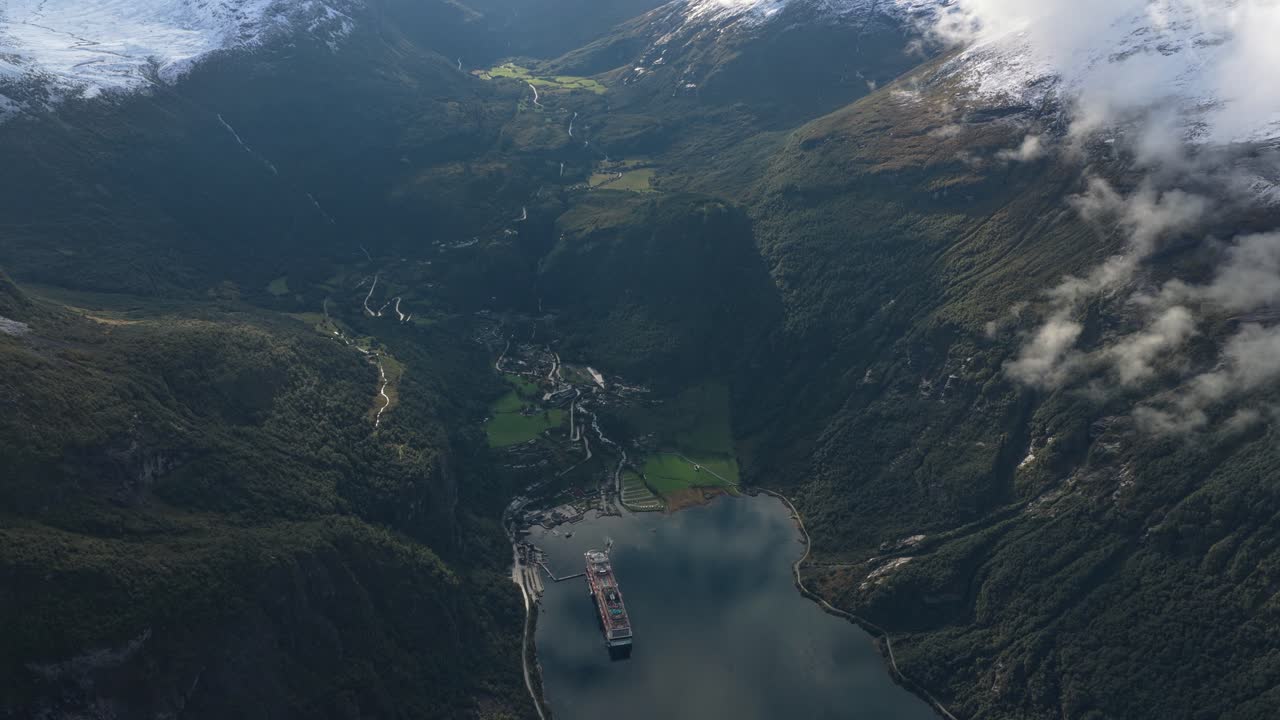 Schneebedeckte Berge erheben sich hinter dem Dorf Geiranger, Luftaufnahme, Norwegen