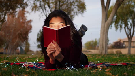 Eine-Junge-Hispanische-Frau,-Die-Ein-Buch-Liest-Und-Ihre-Fantasie-Einsetzt,-Um-Die-Geschichte-Draußen-Im-Park-Bei-Sonnenuntergang-Zum-Leben-Zu-Erwecken