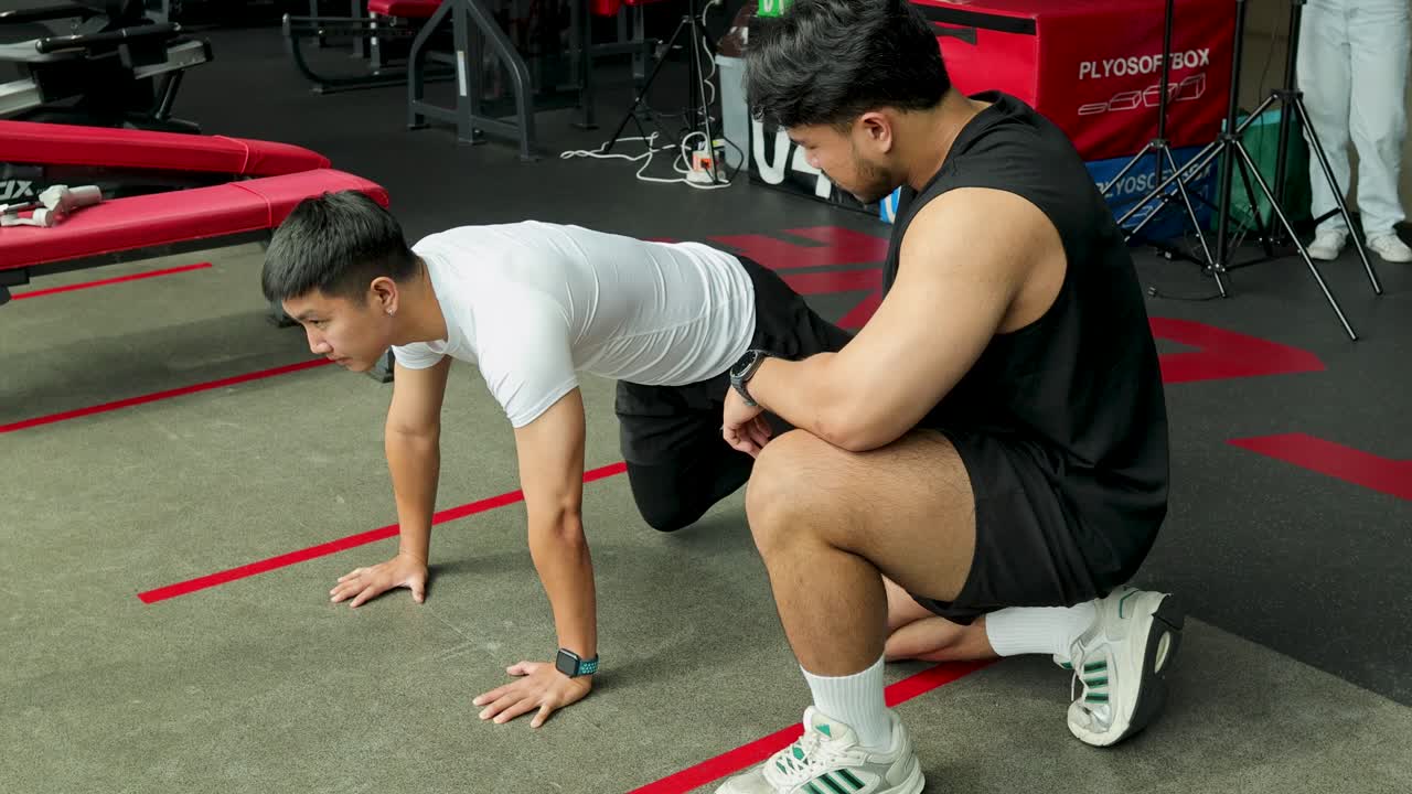 Personal trainer supervises client doing mountain climbers in modern gym with natural lighting