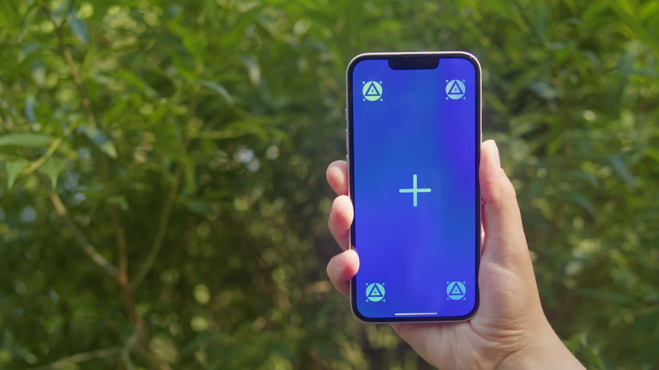 Young woman holding phone chroma key screen in front of green trees in the park close-up. Girl with green screen on smart phone. Nature