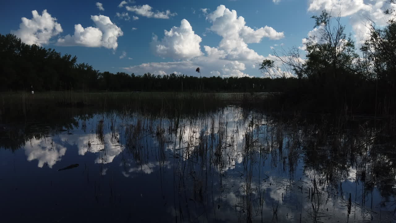 Wide shot of clouds mirrored in the wetlands water surface with a slight tilt up to reveal more of the sky