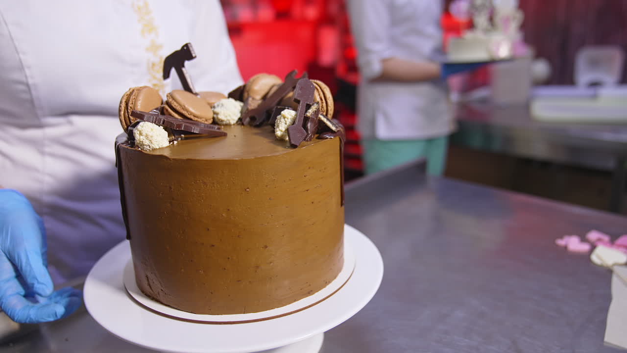 Pastry cook rotates beautiful chocolate cake on the stand. Ready-made dessert product manufactured at the confectionary. Close up.