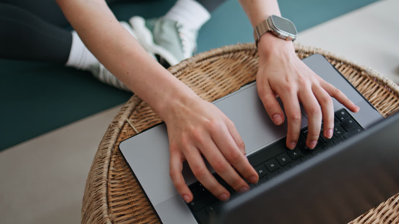 Woman hands typing laptop at wicker table apartment closeup. Unrecognizable girl