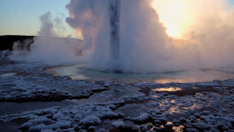 geyser erupting with steam and ice at sunset or sunrise