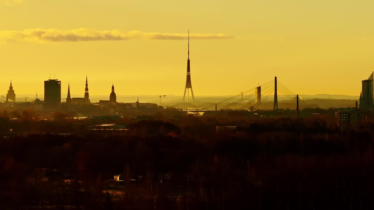 Drone moves sideways showing Riga’s skyline silhouettes glowing in sunrise haze