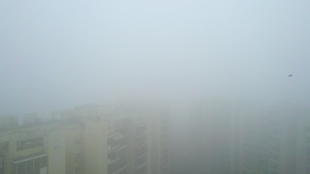 Aerial drone shot flying in between buildings with birds circling and surrounded by dense zero visibility fog during winters in Delhi