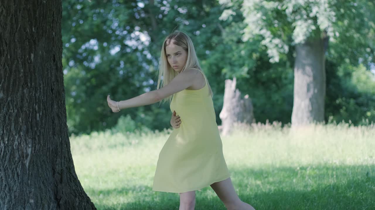 아름다운 젊은 소녀가 자유의 춤을 추고 있습니다. 여름 공원에서 뒷면에 나무가 있습니다.