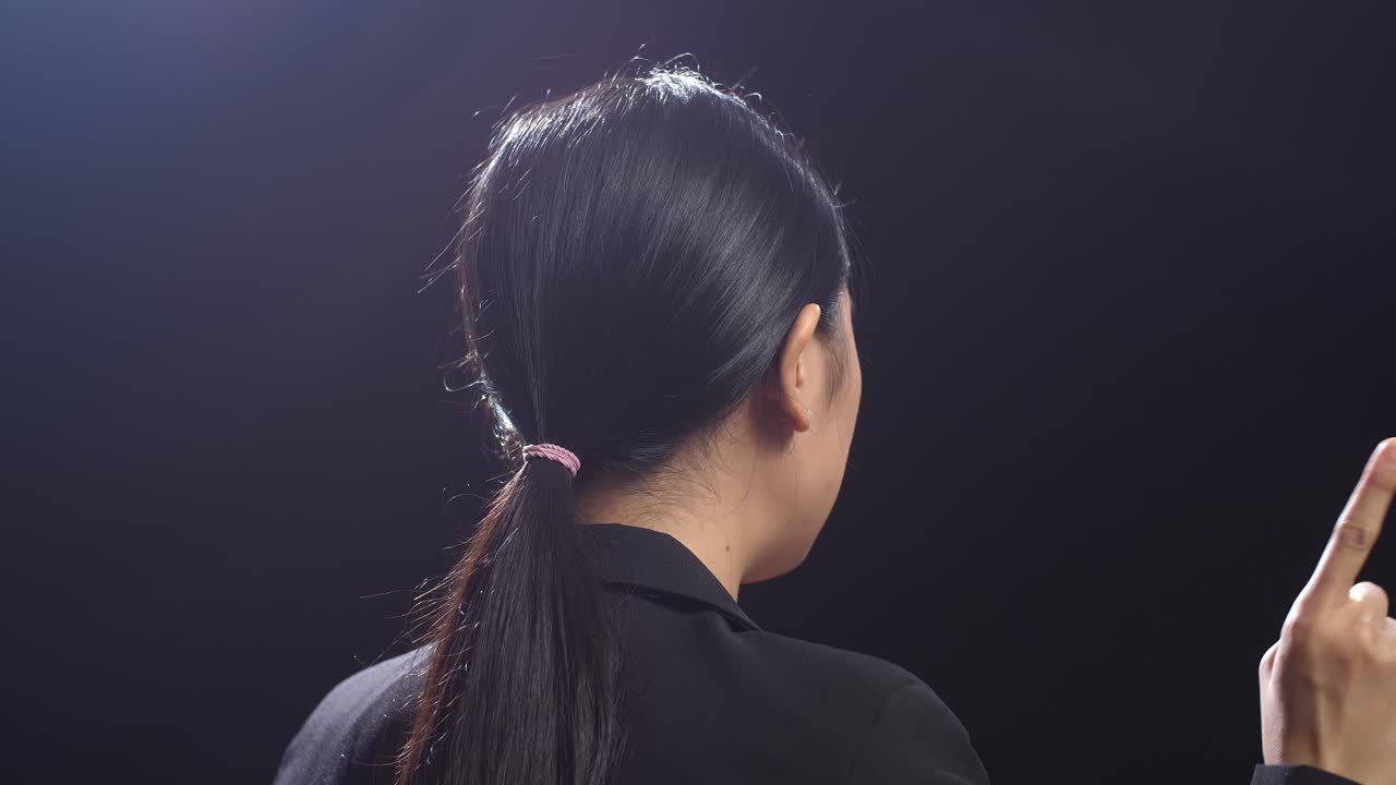 블랙 스크린 스튜디오에서 말하는 동안 지표손가락을 보여주는 비즈니스 슈트를 입은 아시아 스피커 여성의 측면 시각