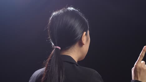 side view of asian speaker woman in business suit showing index fingers up while speaking in the black screen studio