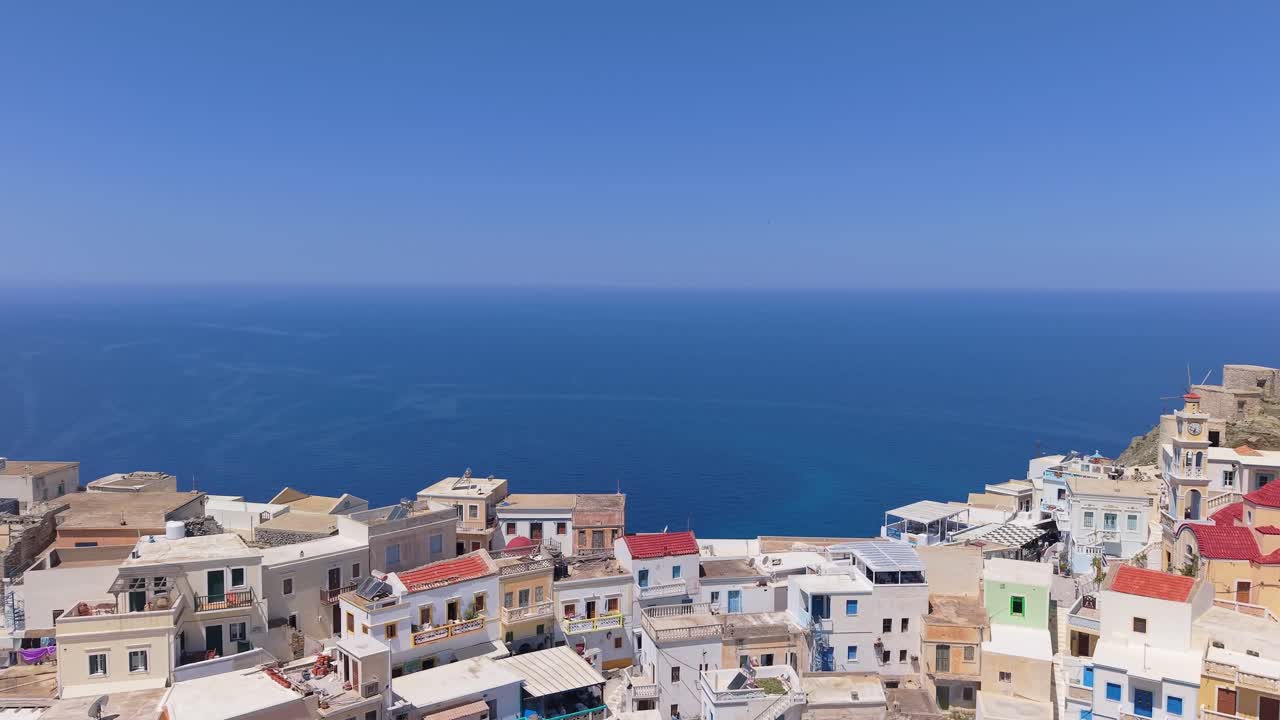 Drone pullback movement from the blue Aegean Sea reveals the traditional and colorful village of Olympos in Karpathos, surrounded by mountains and stunning coastal scenery