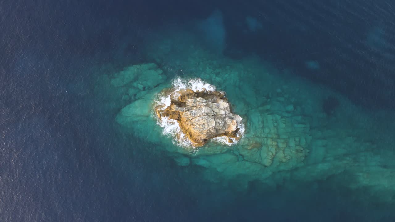 vista aérea de arriba hacia abajo de las olas que se estrellan suavemente en un aislado islote rocoso en grecia