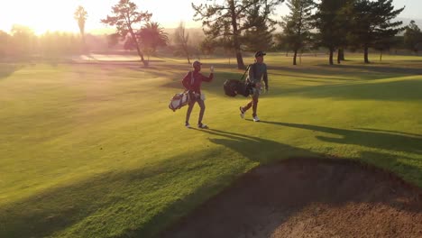 Two-diverse-male-golf-players-walking-at-golf-course-on-sunny-day