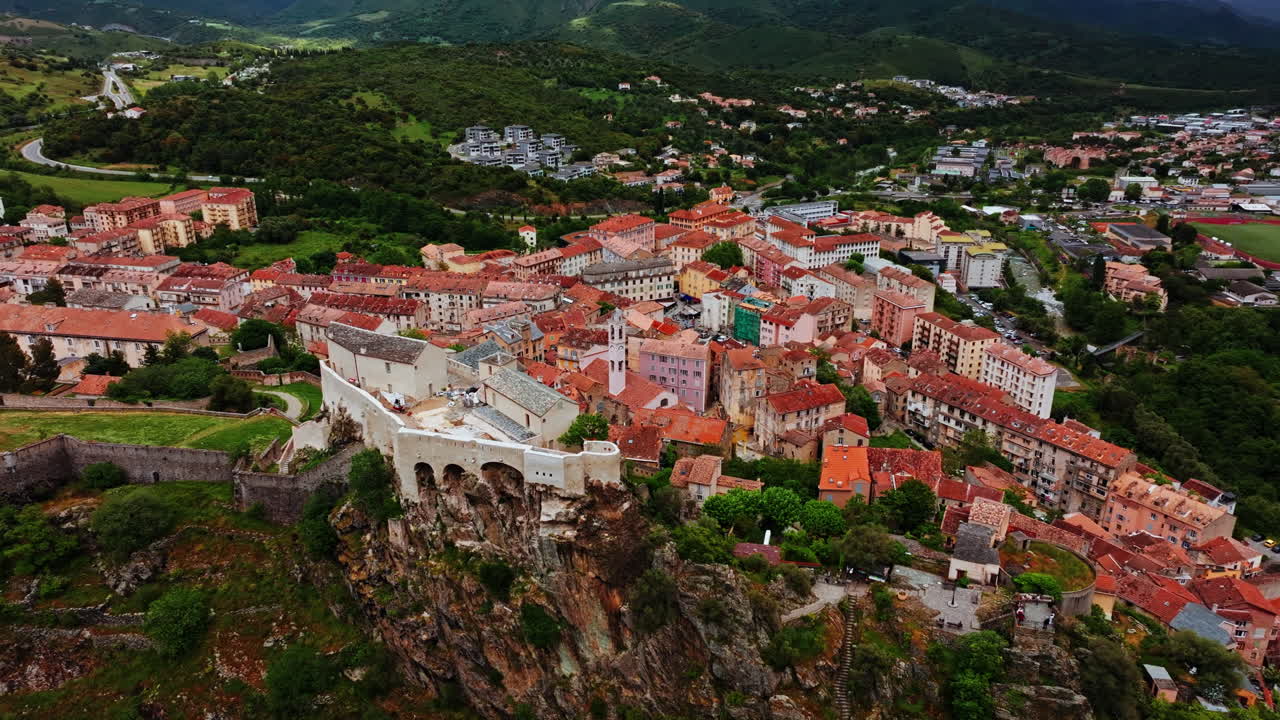 Aerial drone shot over the historic town of Corte, Corsica, France. High view of the old town and fortress overlooking the landmark on top of the hill. View of the scenic landscape and mountains