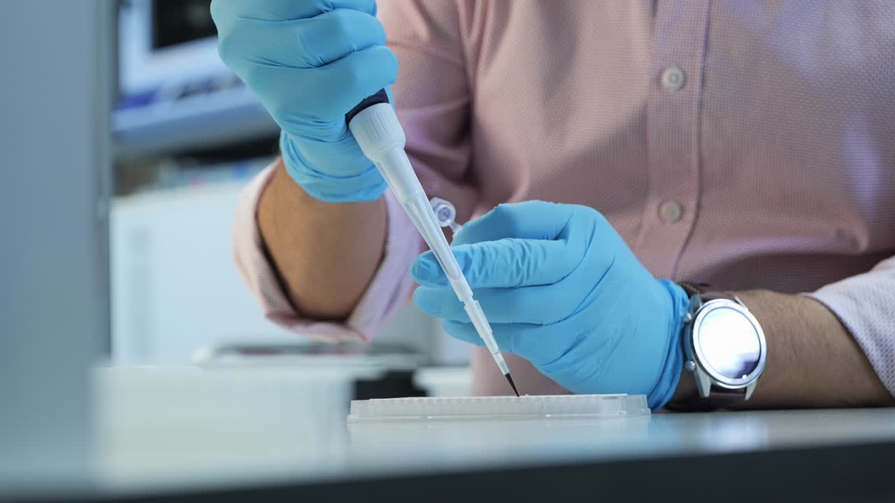 Close-up of a scientist or lab technician manipulating a micropipette to transfer liquid into a well plate