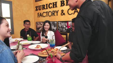 waiter serving pizza to friendly asian group of friends at restaurant , full hd