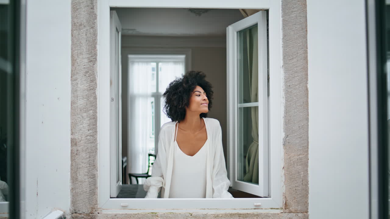 Black hair girl waving window morning house. Curly smiling woman peeping outside