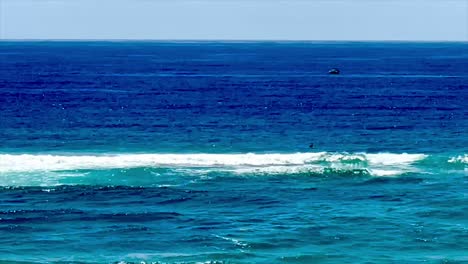 Lone-surfer-sitting-out-the-back-in-deep-blue-ocean-with-boat-in-view-on-the-Gold-Coast,-Queensland,-Australia