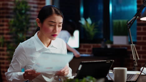 Businesswoman-crosschecking-data-between-financial-charts-and-laptop