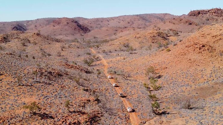 Nelivetoiset ajoneuvot etenevät vaivalloisesti pölyisellä tiellä Australian takamailla.
