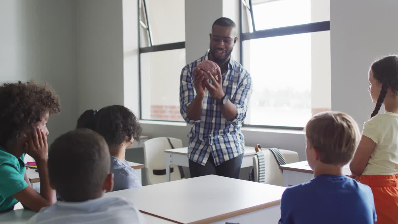 Video of happy african american male teacher and class of diverse pupils during biology lesson