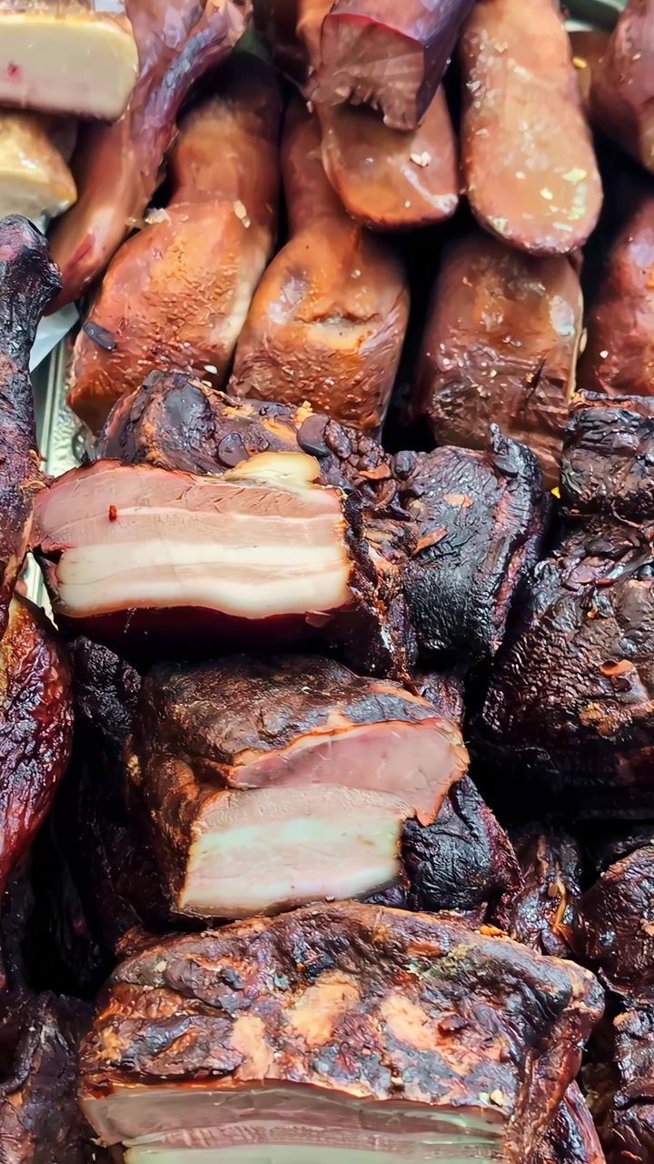 Wędzone plastry boczku wieprzowego, peklowany bekon, żeberka i przypalone kawałki mięsa ułożone na tradycyjnym stoisku rzeźniczym, zbliżenie, wideo pionowe, najazd kamery w lewo.