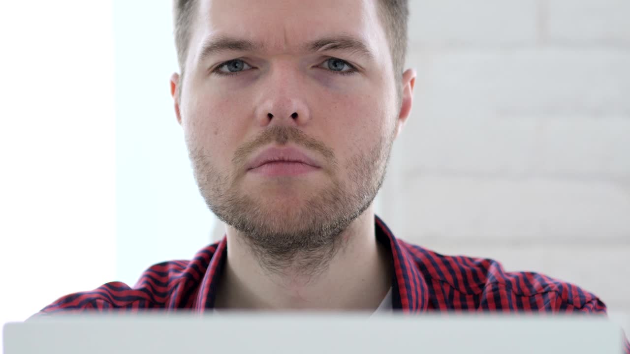 joven mirando a la cámara mientras trabaja en una computadora portátil